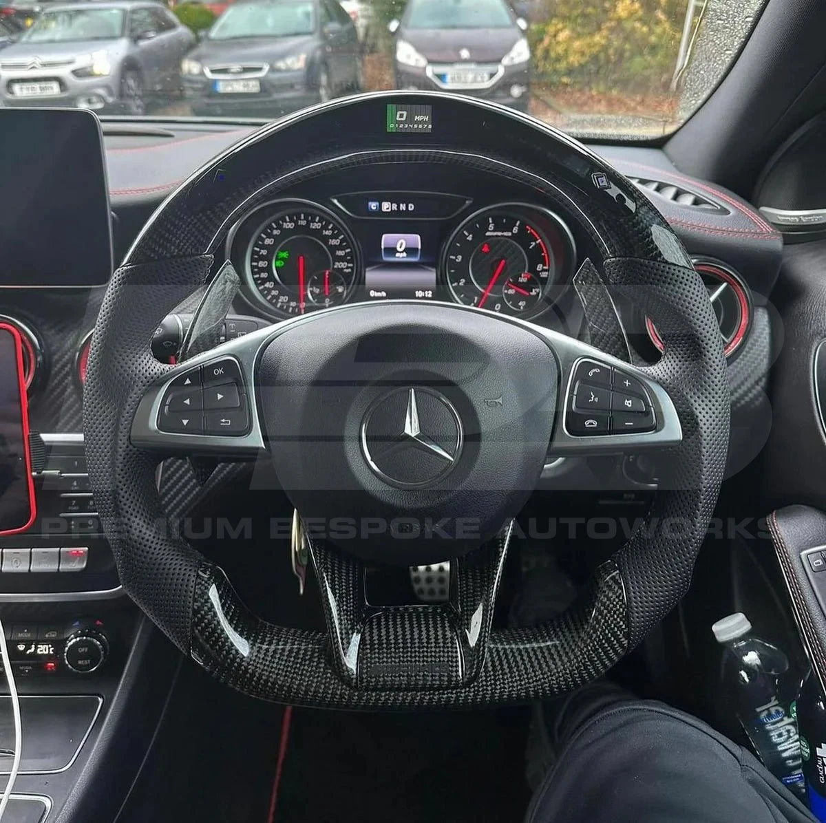 Car interior with steering wheel featuring Mercedes-Benz logo, dashboard, and visible brand logos.