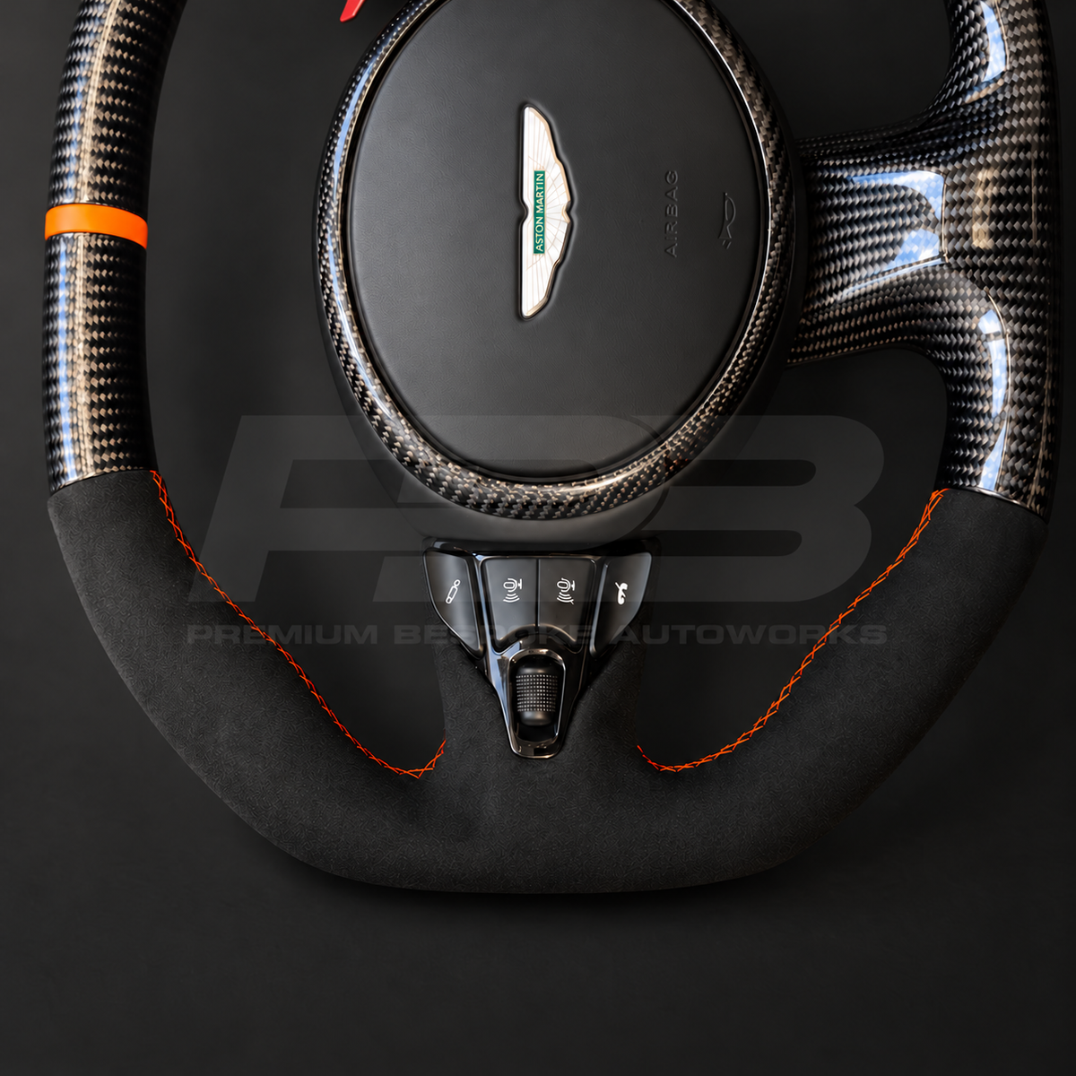 Aston Martin Vantage Facelift custom steering wheel close up detail showing flat top and bottom, gloss carbon fibre, black Alcantara grips, orange stitching and orange marker