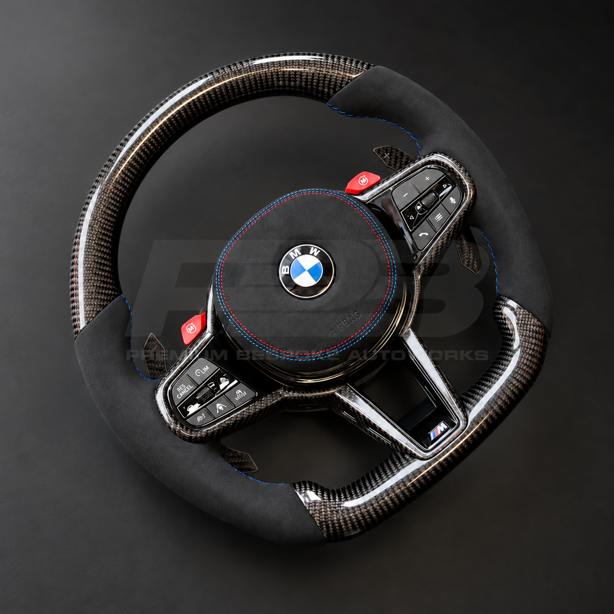 BMW M3 G80 LCI custom steering wheel left angle showing flat bottom, gloss carbon fibre top, bottom and trims, black Alcantara grips and airbag cover with M tricolour stitching, red M buttons