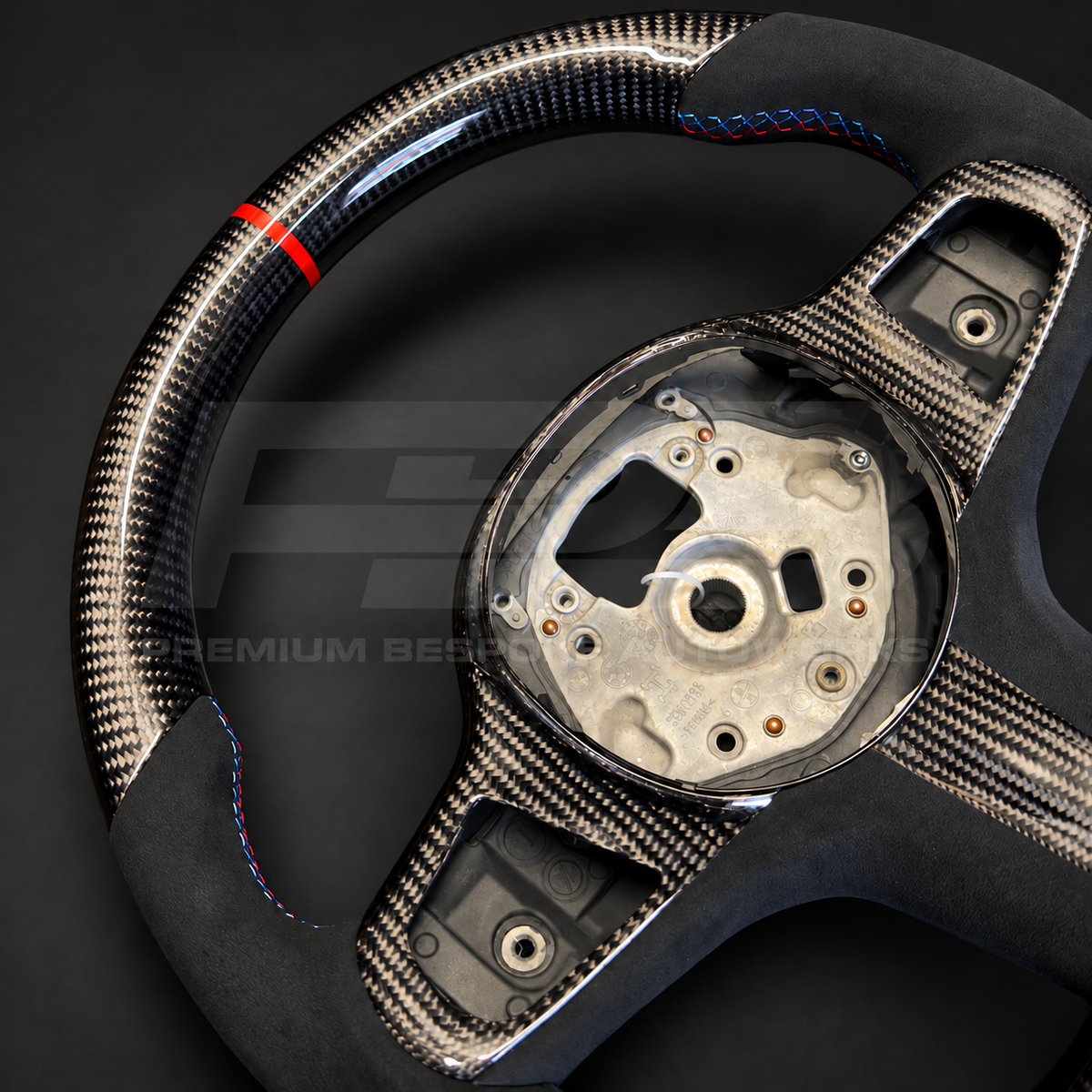 BMW X5 G05 custom steering wheel, close angled view of the carbon fibre weave, red 12 o'clock strip and carbon spoke trims