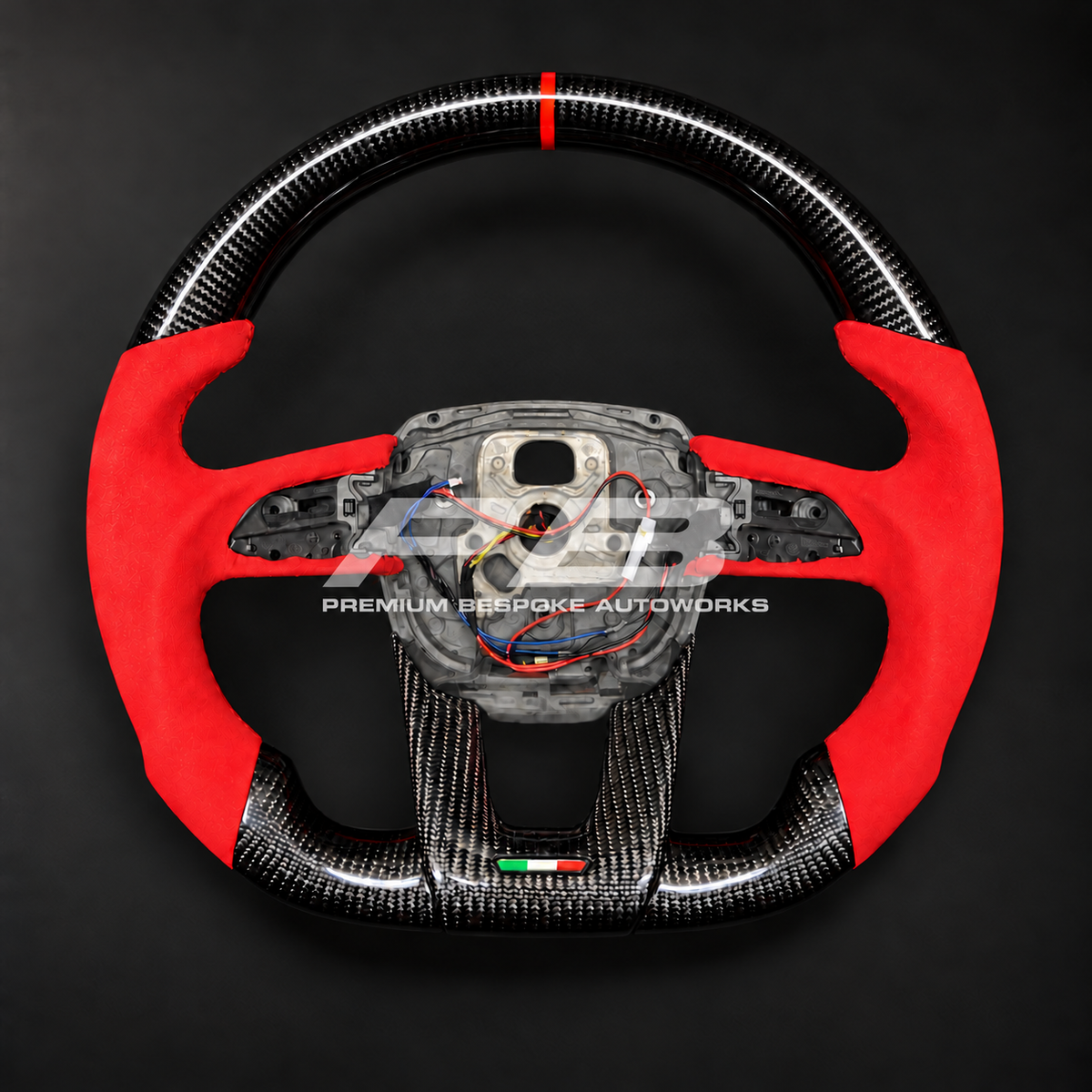 Lamborghini Urus custom steering wheel, front view, flat bottom gloss carbon fibre with red Alcantara grips, red marker and carbon lower trim with Italian flag detail, customer build by Premium Bespoke AutoWorks