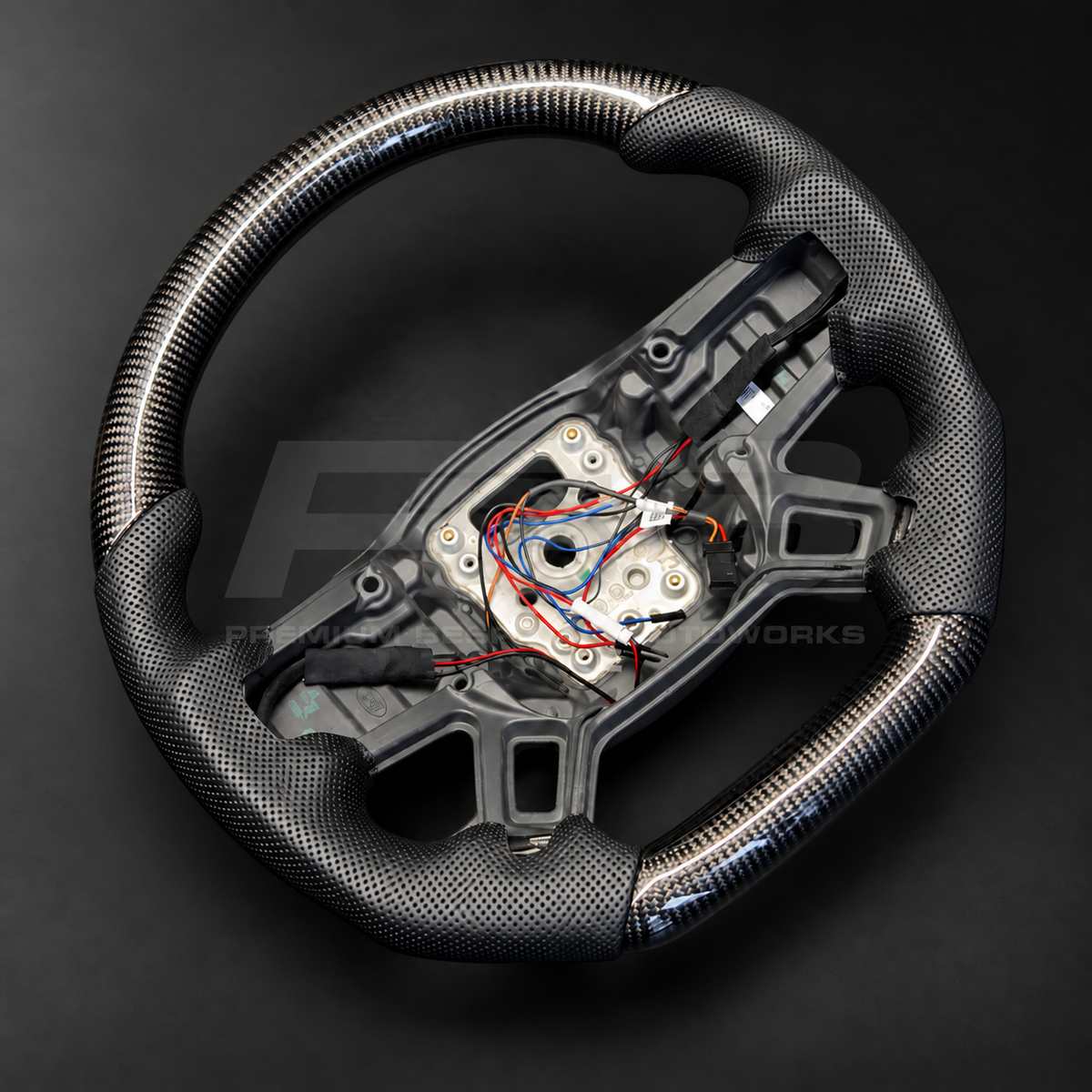 Land Rover Defender L663 custom steering wheel rotated to show the gloss carbon fibre top section and perforated leather grips