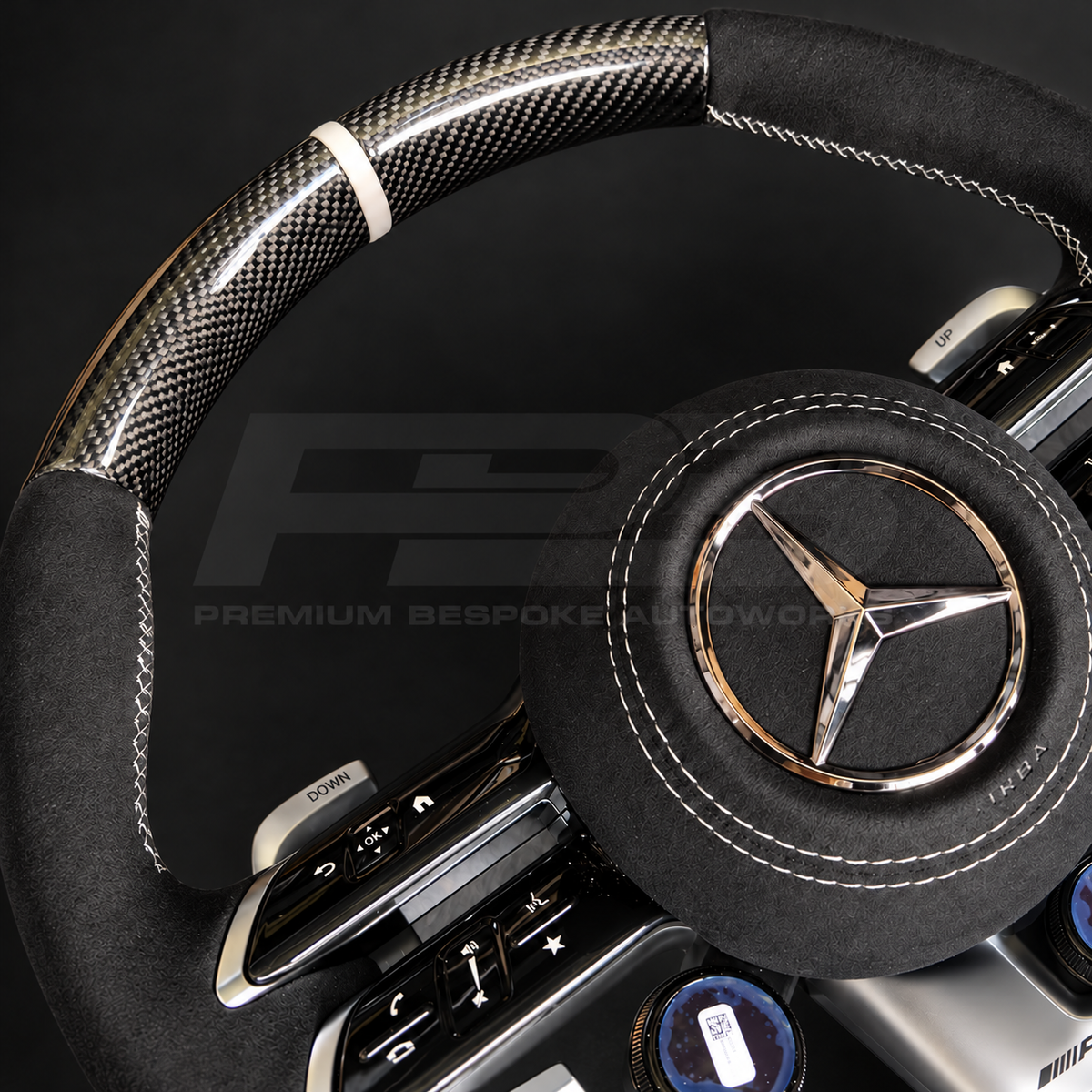 Mercedes-AMG G63 custom steering wheel close up detail showing gloss carbon fibre top and bottom, black Alcantara grips and airbag cover, classic grey stitching and marker, AMG drive unit dials
