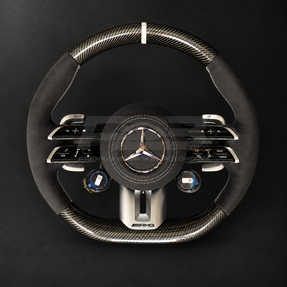 Mercedes-AMG G63 custom steering wheel left angle showing gloss carbon fibre top and bottom, black Alcantara grips and airbag cover, classic grey stitching and marker, AMG drive unit dials