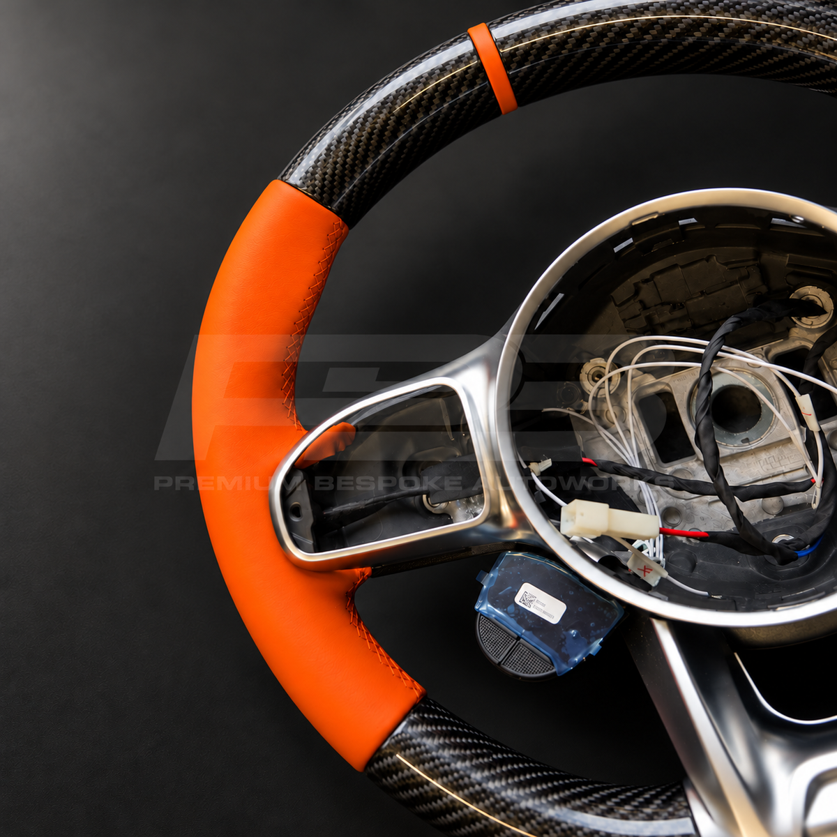 Mercedes-AMG G63 W463 Facelift custom steering wheel close up detail showing gloss carbon fibre top and bottom, orange leather grips and orange 12 o'clock marker
