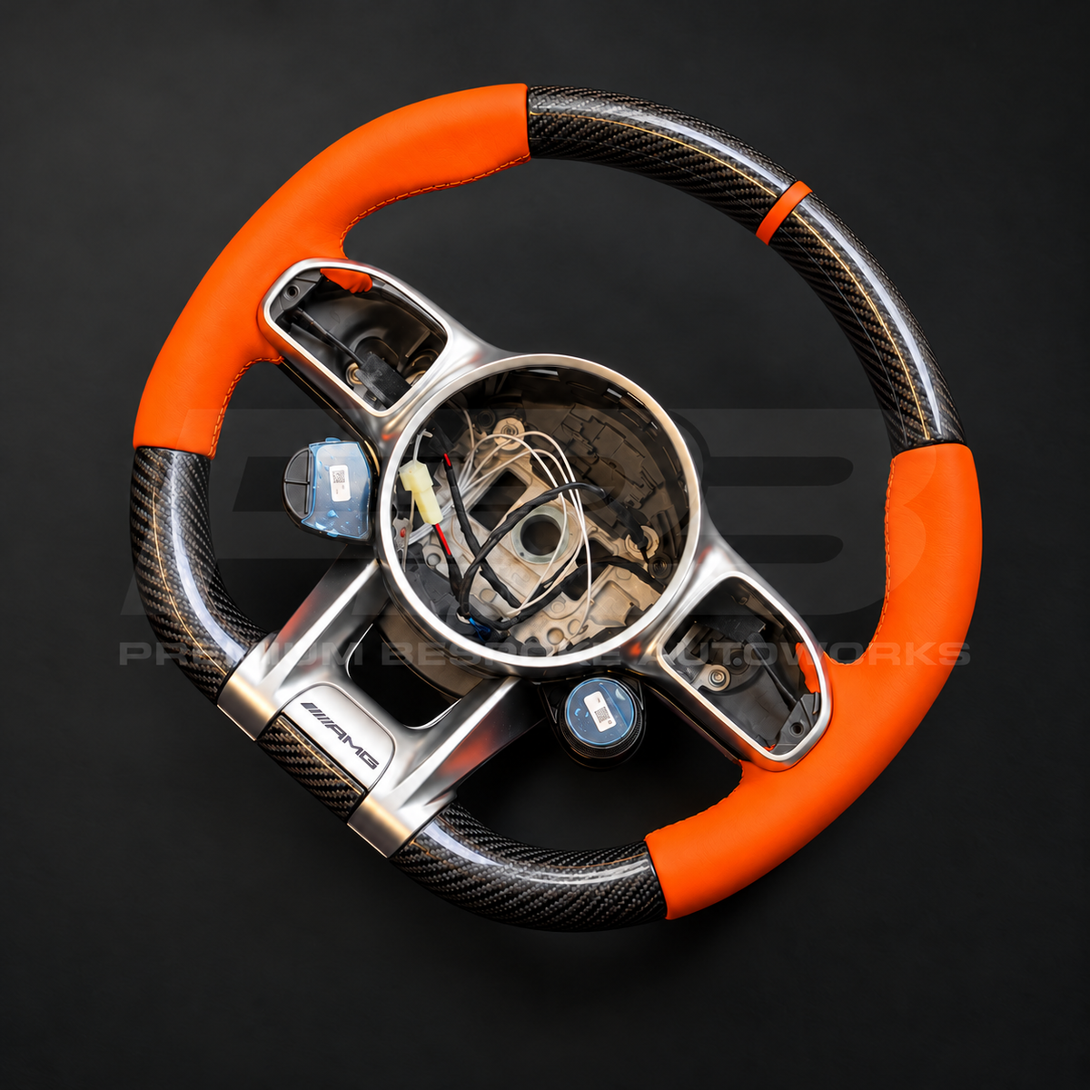 Mercedes-AMG G63 W463 Facelift custom steering wheel left angle showing gloss carbon fibre top and bottom, orange leather grips and orange 12 o'clock marker