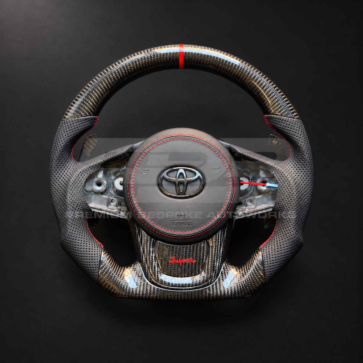 Toyota GR Supra MKV custom steering wheel as built, flat bottom, gloss carbon fibre with red 12 o'clock marker, perforated leather grips, red stitching, leather airbag cover, carbon trims with red Supra script, magnetic paddles