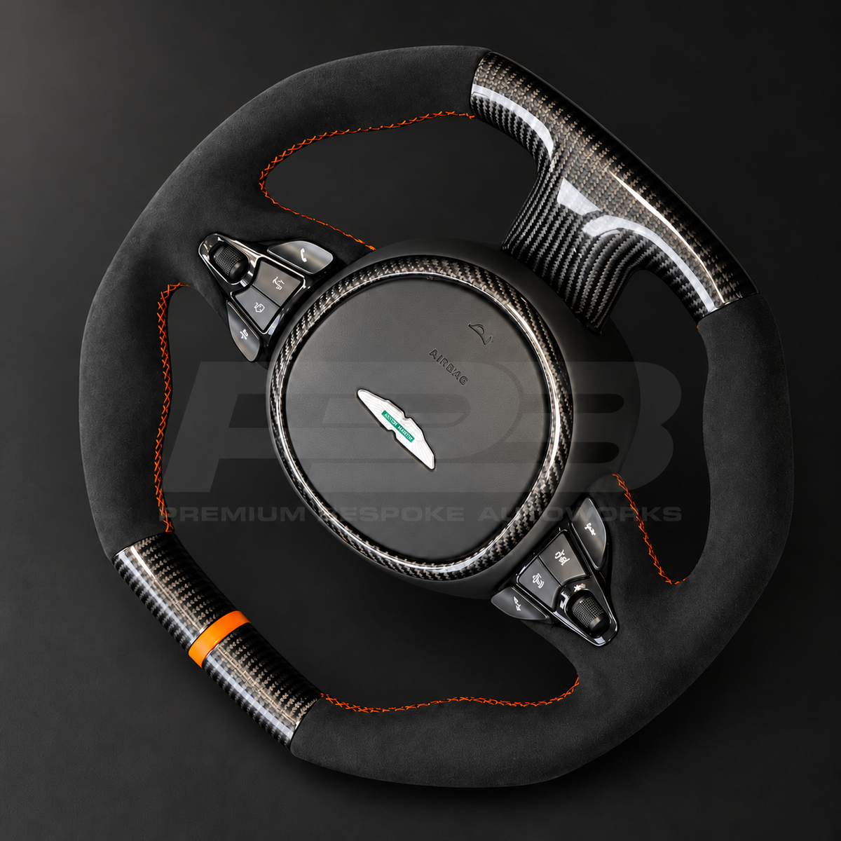 Aston Martin Vantage Facelift custom steering wheel angled view showing flat top and bottom, gloss carbon fibre, black Alcantara grips, orange stitching and orange marker