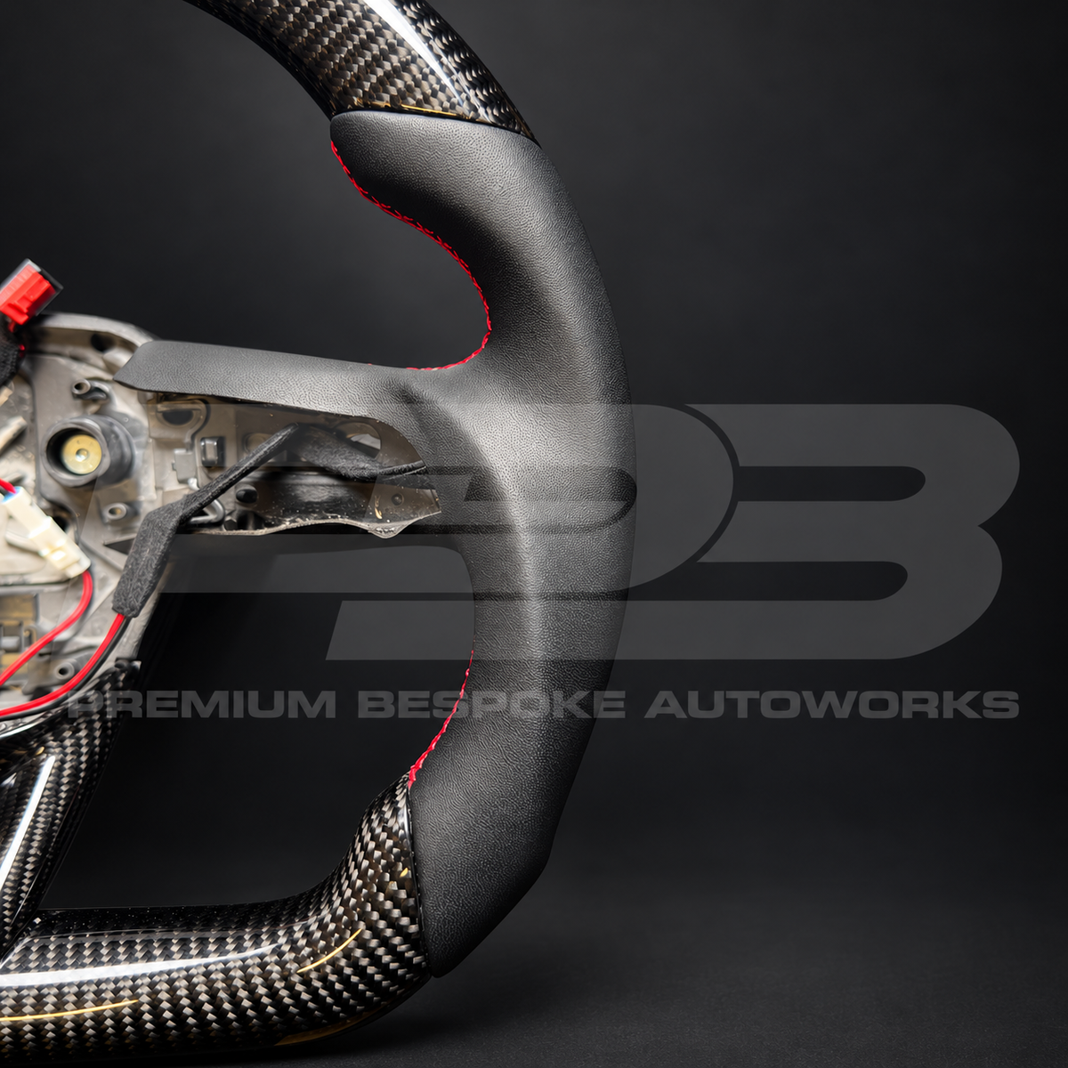 Audi RS Q8 custom steering wheel from the side, showing the flat bottom carbon fibre rim and red stitched black leather grip