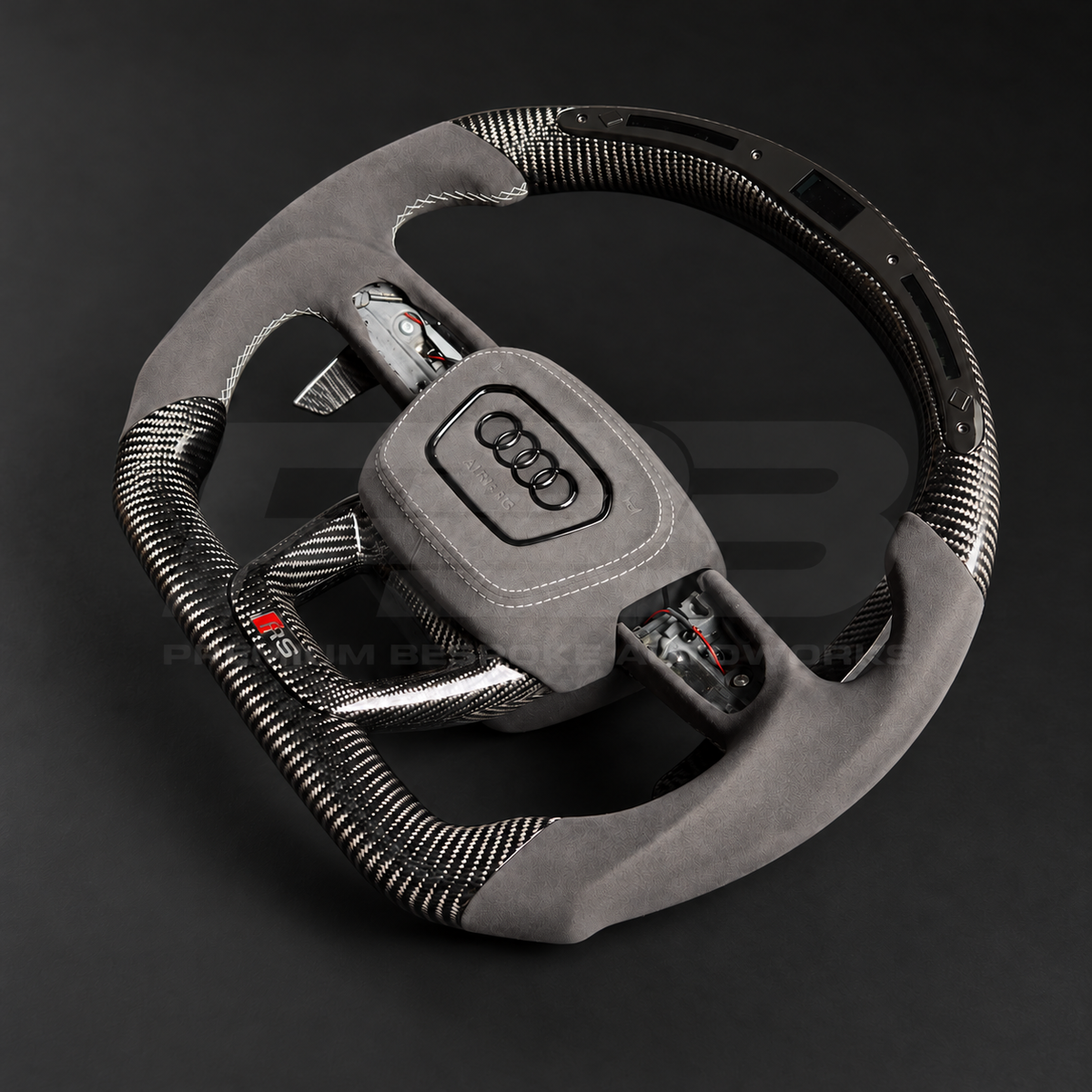 Audi RSQ8 custom steering wheel right angle showing flat top and bottom, gloss carbon fibre, RPM race display, grey Alcantara grips and airbag cover, carbon paddles