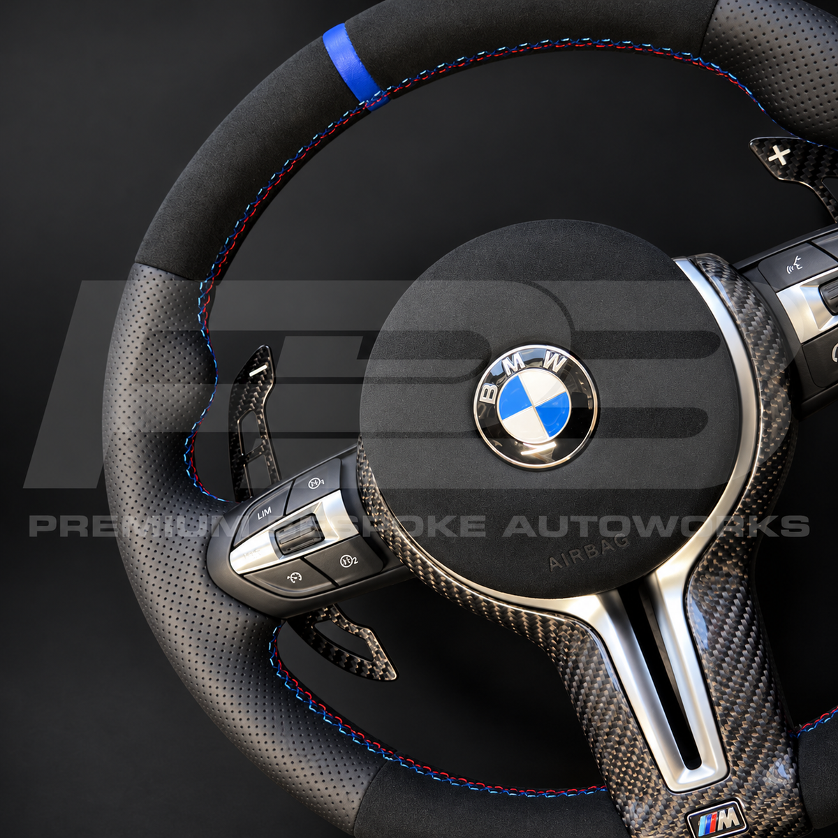 BMW M3 F80 Alcantara custom steering wheel at an angle, showing the blue 12 o'clock marker, M tricolour stitching, carbon button surrounds and magnetic paddles