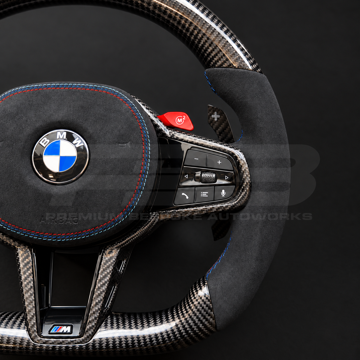 BMW M3 G80 LCI custom steering wheel close up detail showing flat bottom, gloss carbon fibre top, bottom and trims, black Alcantara grips and airbag cover with M tricolour stitching, red M buttons