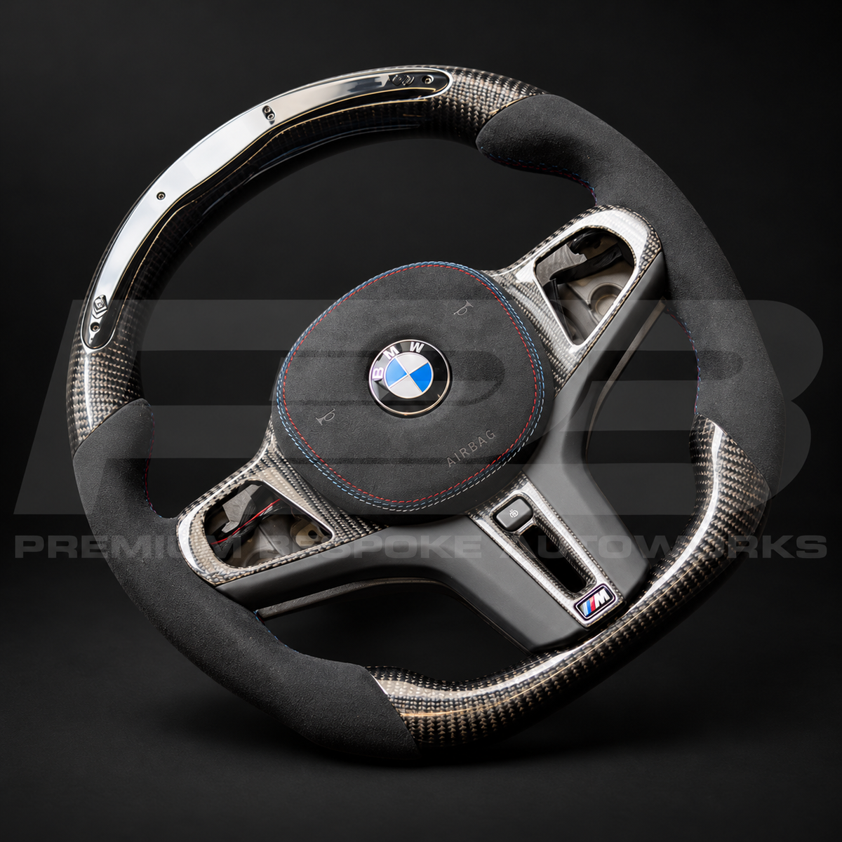 BMW M4 G82 custom steering wheel angled from the left, showing the carbon fibre spoke trims, black Alcantara grip and RPM display