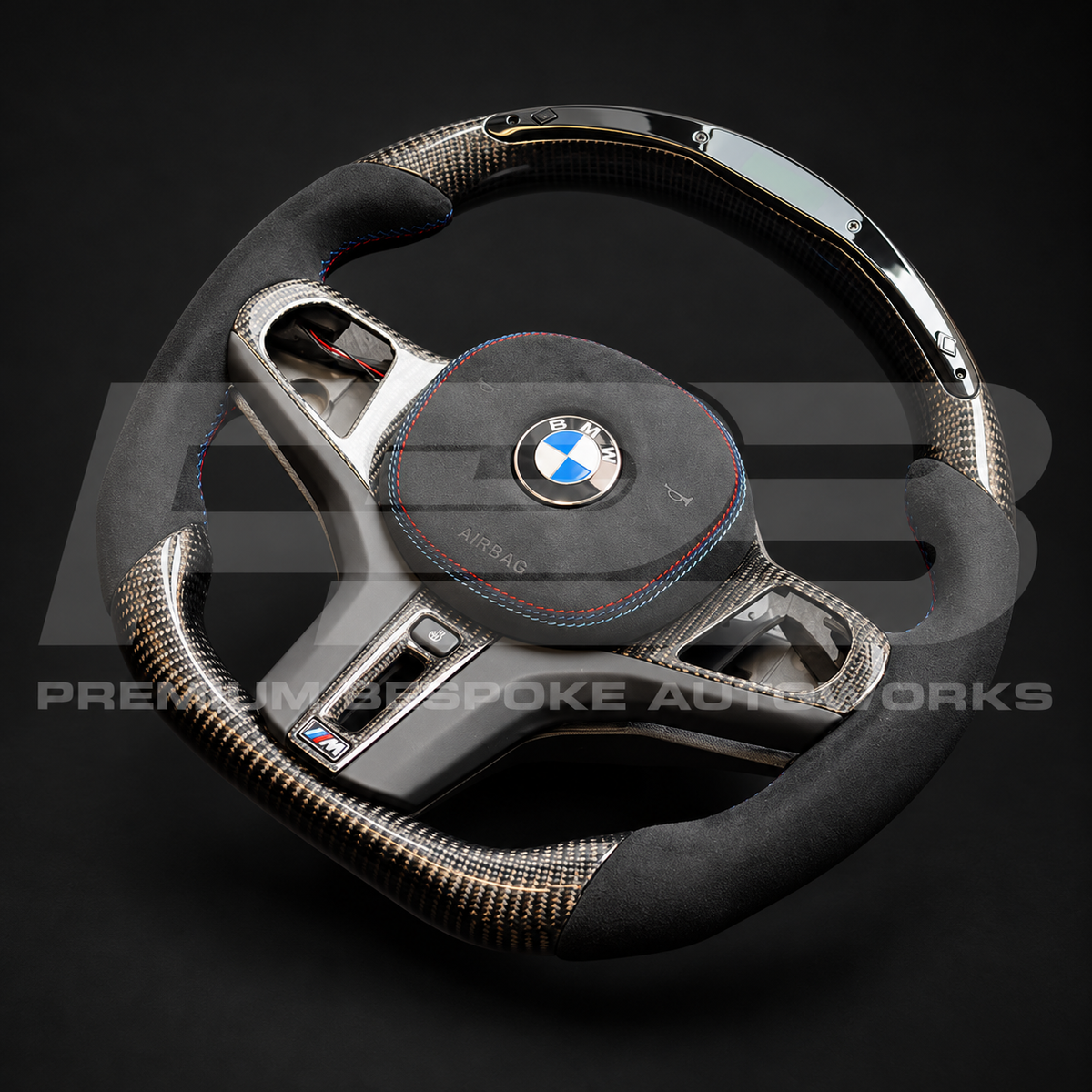 BMW M4 G82 custom steering wheel angled from the right, gloss carbon fibre top and bottom with black Alcantara grips and M tricolour stitching