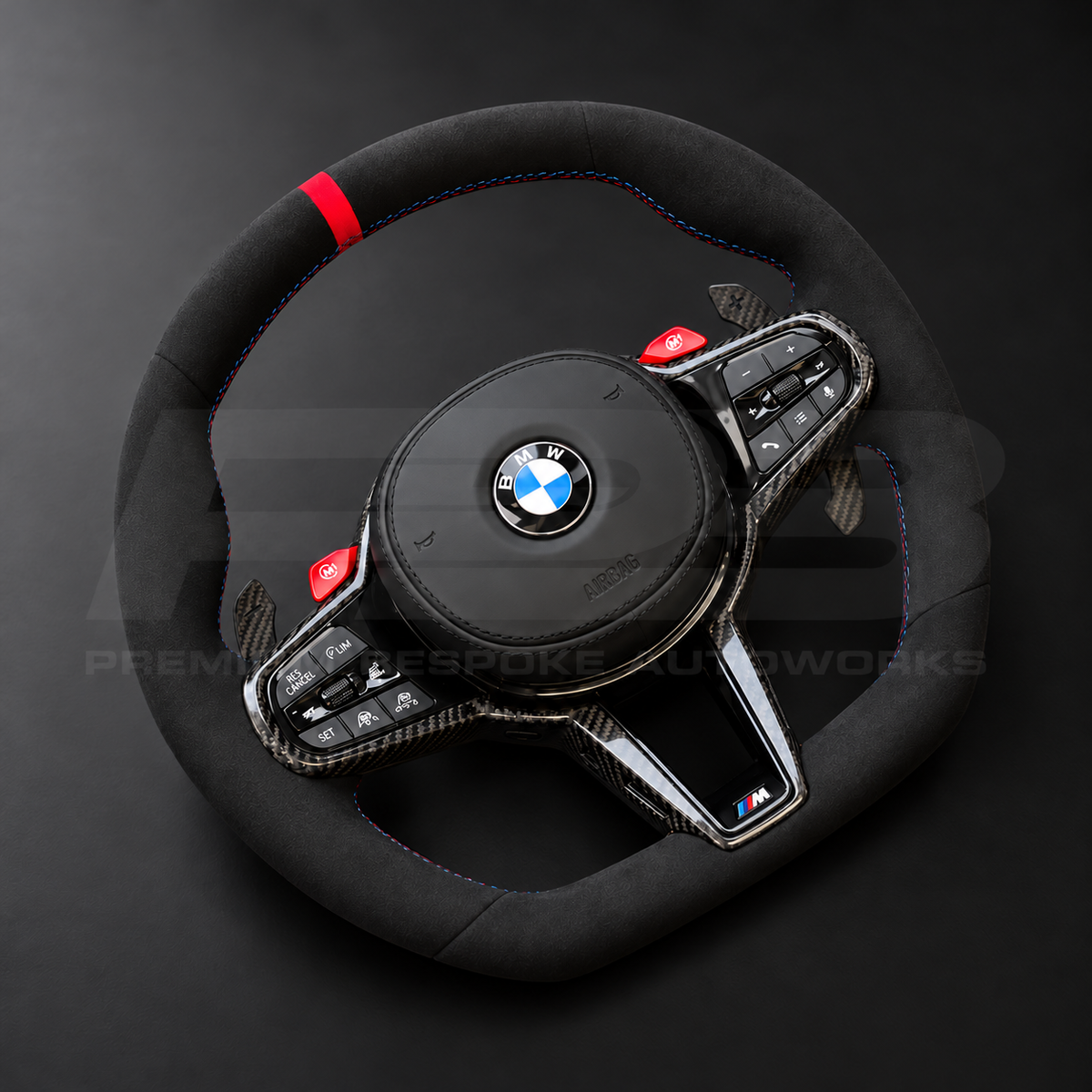 BMW M4 G82 LCI custom steering wheel left angle showing full black Alcantara, red 12 o'clock marker, M tricolour stitching, Alcantara airbag cover, carbon trims, red M buttons