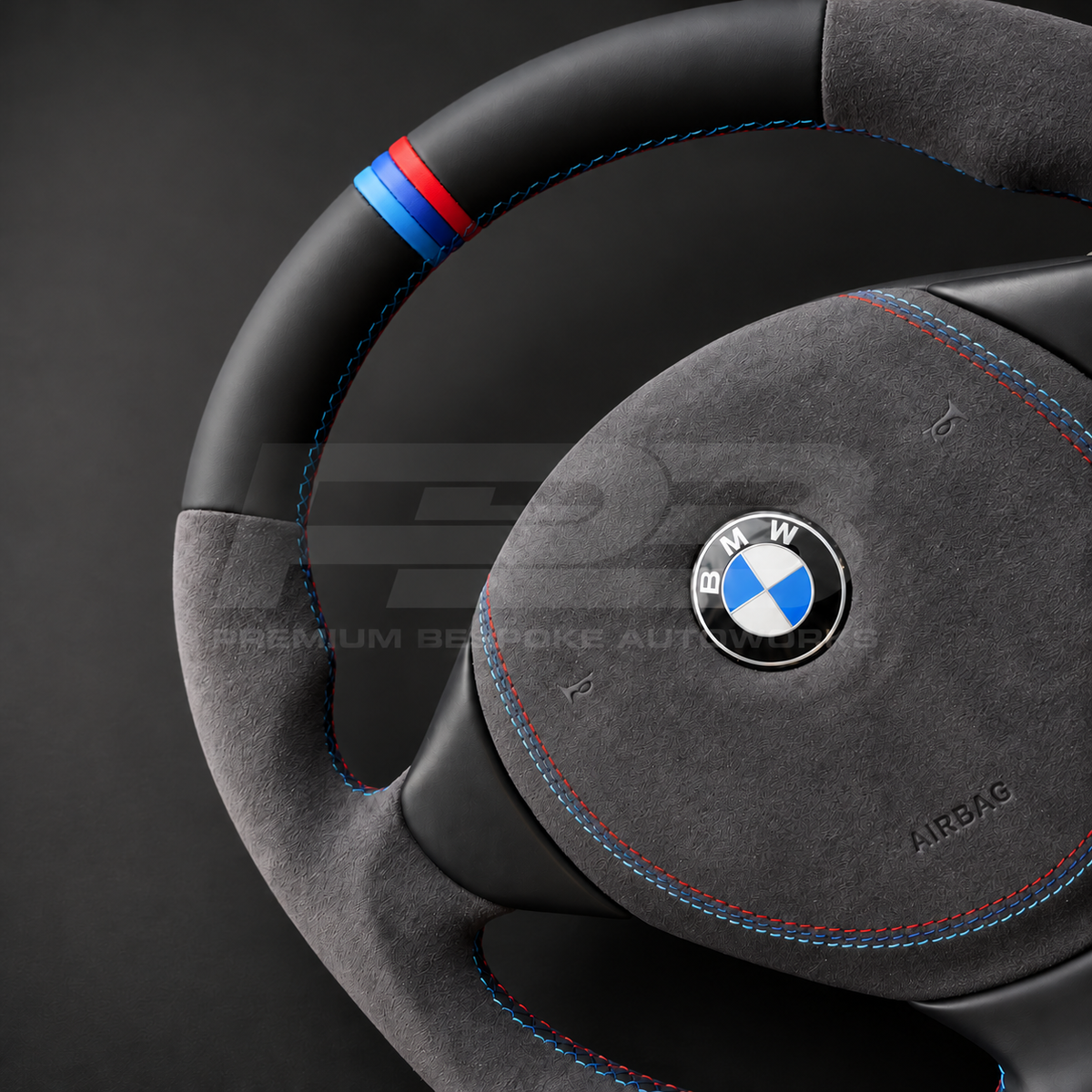 BMW Z3 custom steering wheel close up detail showing flat bottom, black leather top and bottom, dark grey Alcantara grips and airbag cover, M stitching and M stripe
