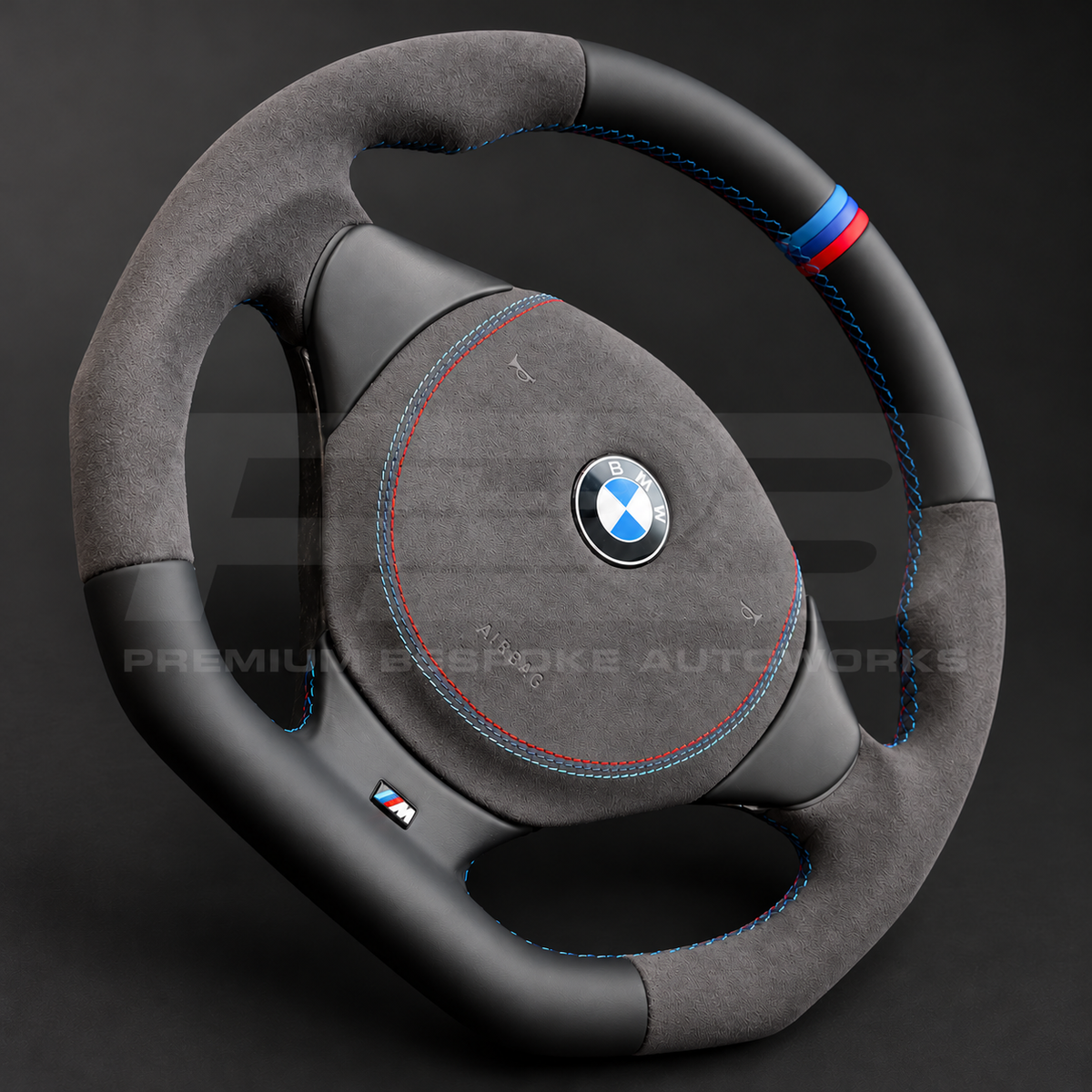 BMW Z3 custom steering wheel close up detail showing flat bottom, black leather top and bottom, dark grey Alcantara grips and airbag cover, M stitching and M stripe