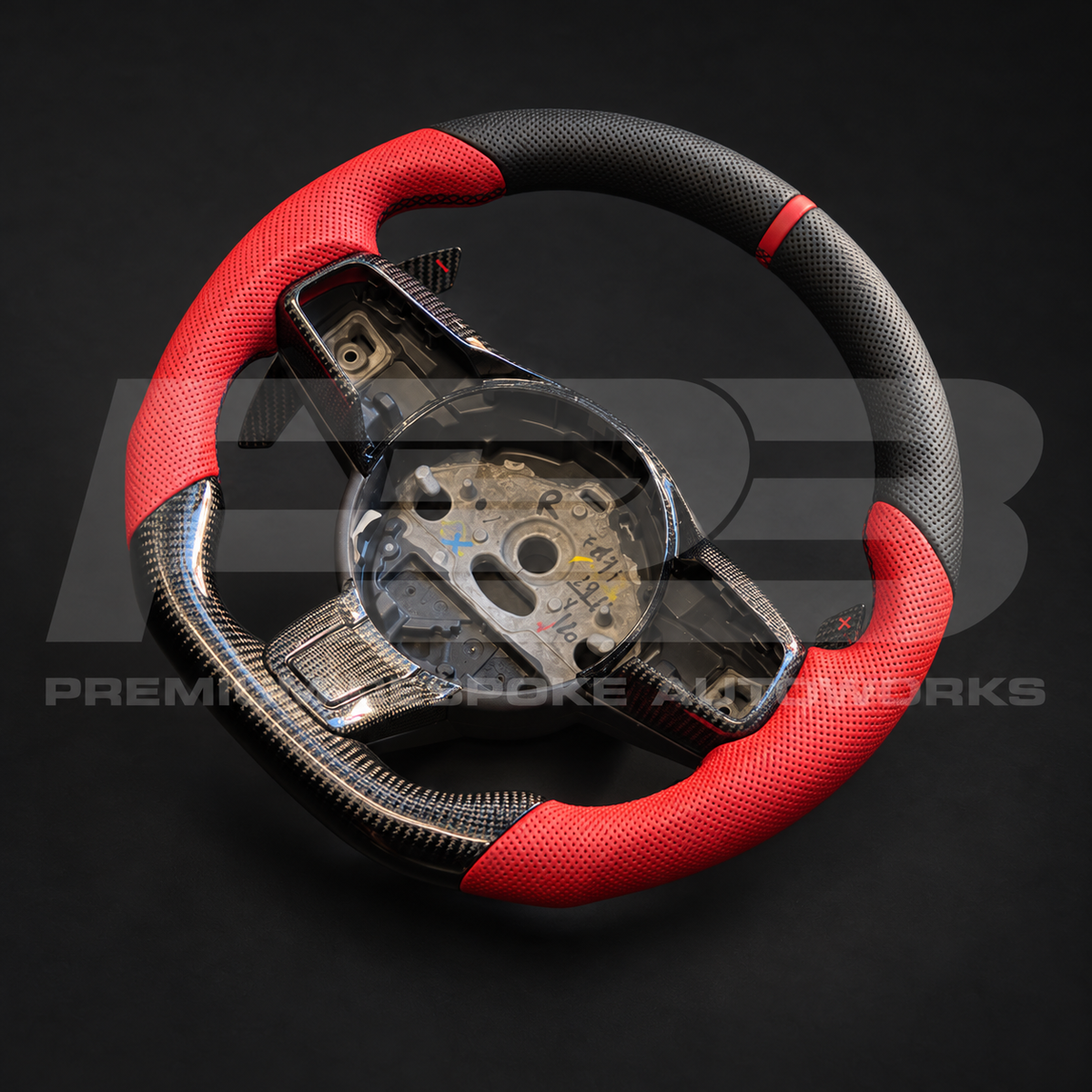 Jaguar F-Type custom steering wheel angled from the right, showing the perforated black leather top, red grips and gloss carbon fibre bottom section