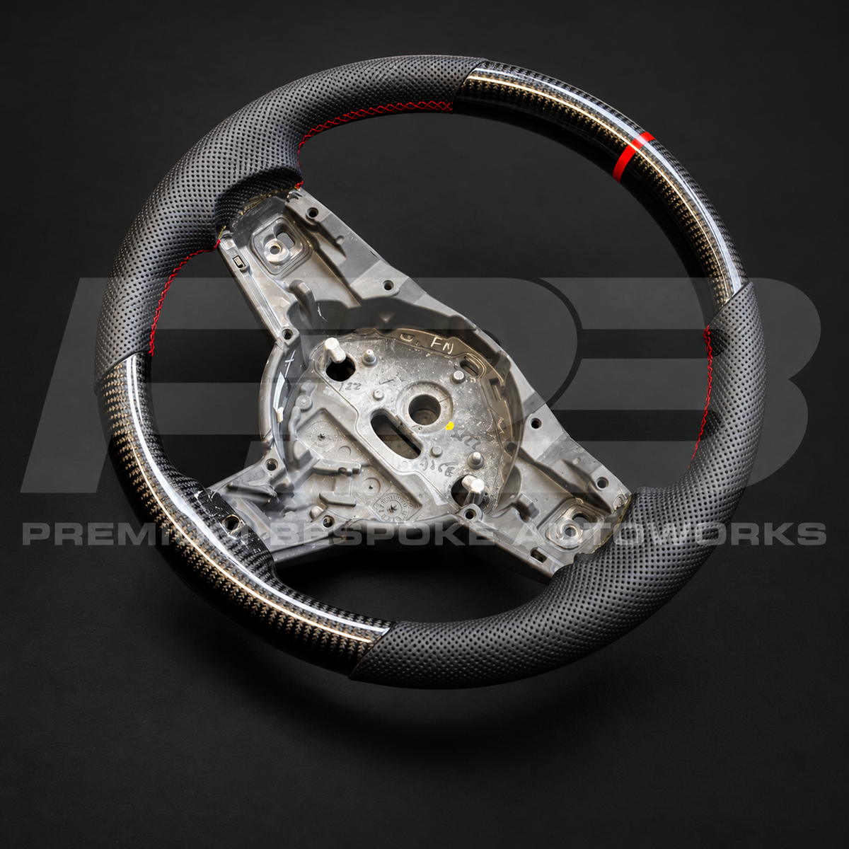 Jaguar F-Type custom steering wheel angled from the right, showing the carbon fibre bottom section and red stitched grips