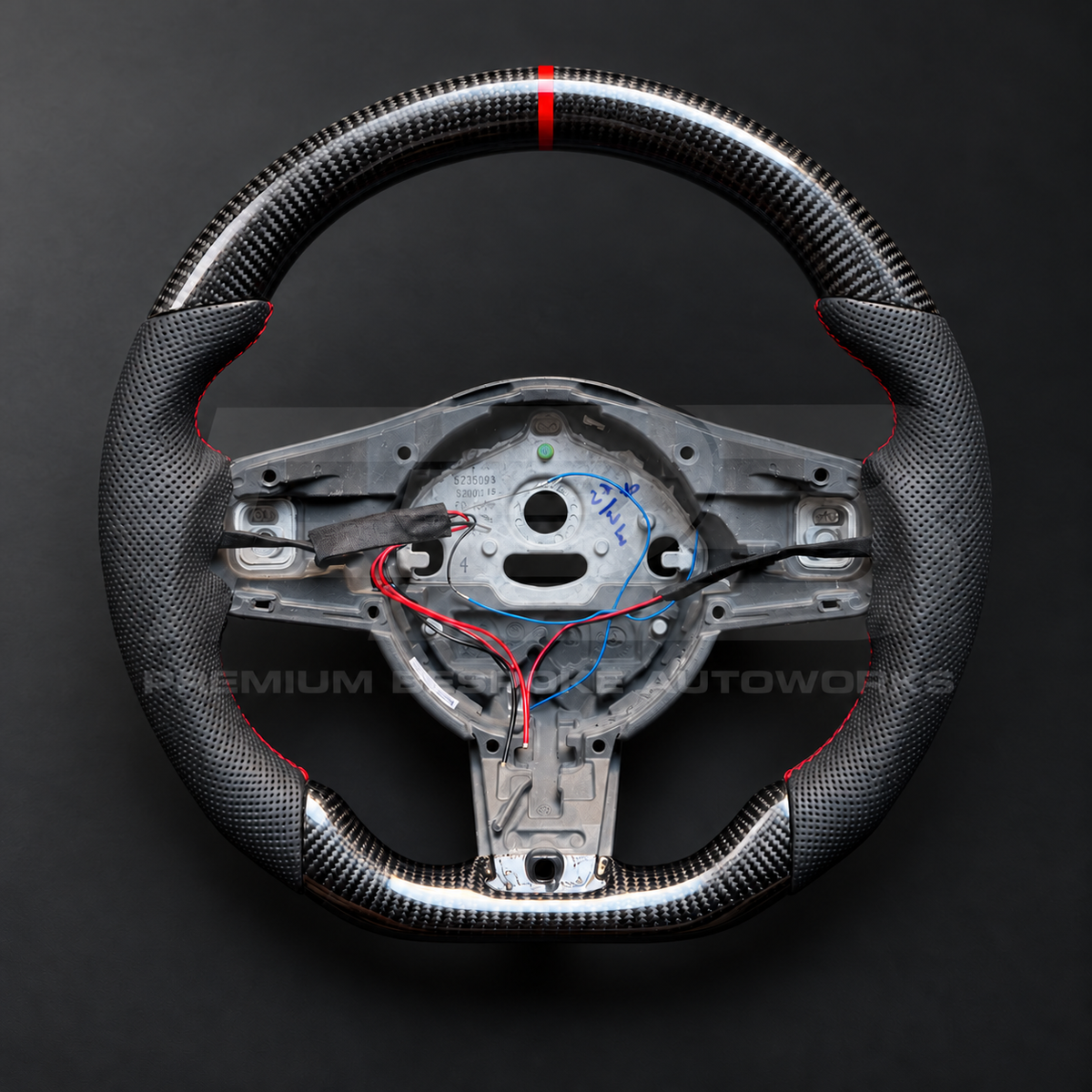 Jaguar F-Type custom steering wheel front view, flat bottom, gloss carbon fibre top and bottom, perforated black grips, red stitching and red 12 o'clock marker