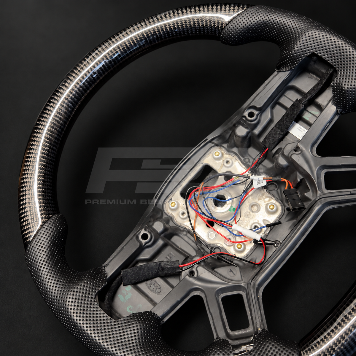 Land Rover Defender L663 custom steering wheel, close angled view of the carbon fibre weave and perforated black leather grip