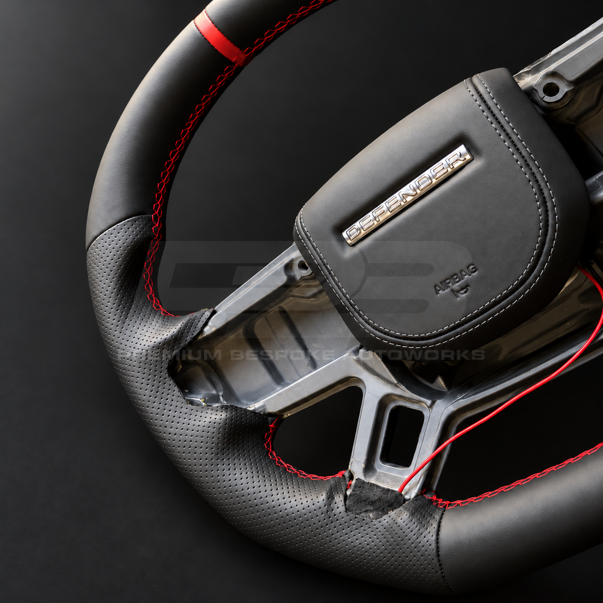 Land Rover Defender L663 custom steering wheel close up detail showing flat bottom, black nappa leather, perforated grips, red stitching and red marker, black leather airbag cover
