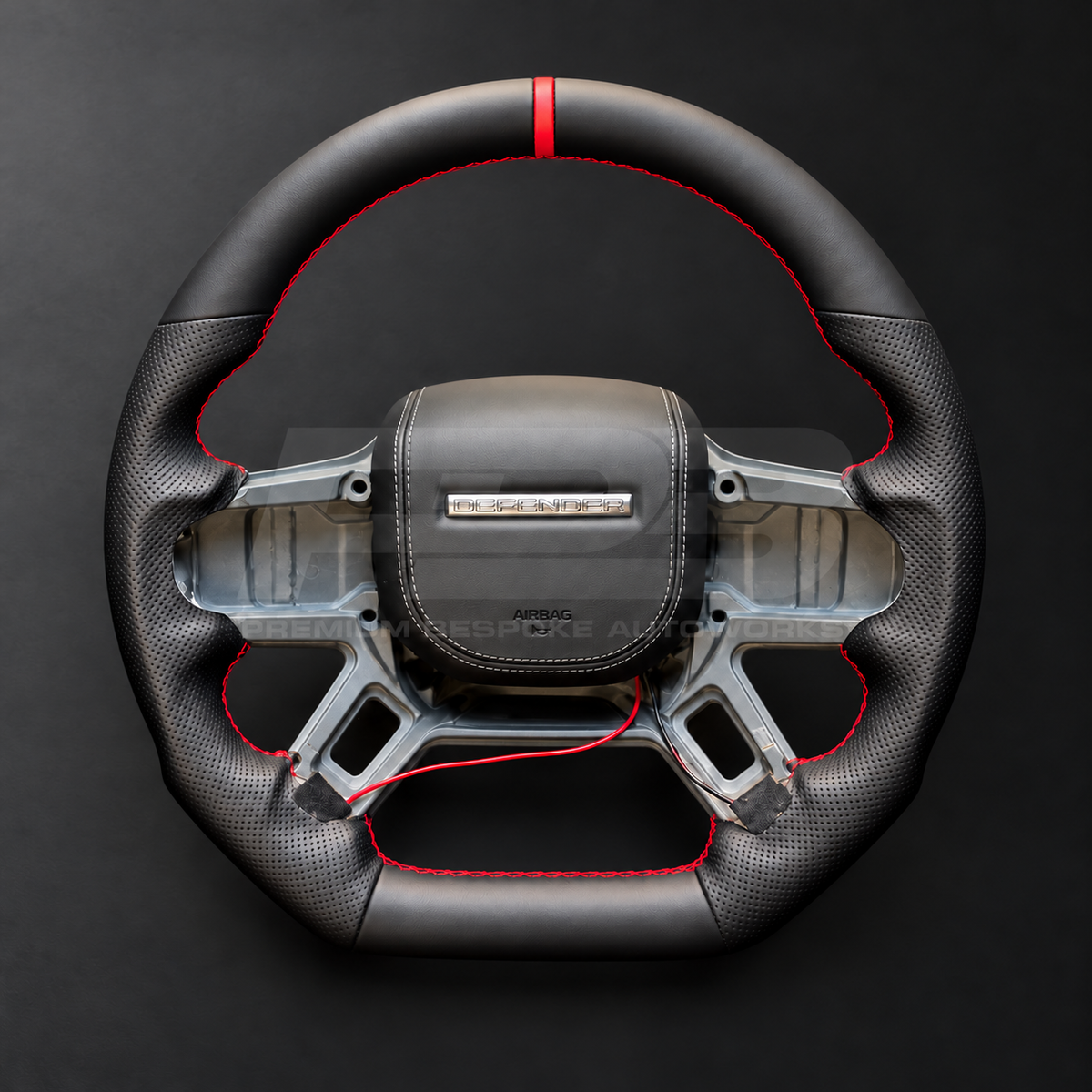 Land Rover Defender L663 custom steering wheel front view, flat bottom, black nappa leather, perforated grips, red stitching and red marker, black leather airbag cover