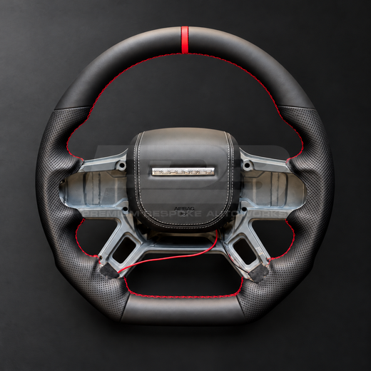 Land Rover Defender L663 custom steering wheel front view, flat bottom, black nappa leather, perforated grips, red stitching and red marker, black leather airbag cover