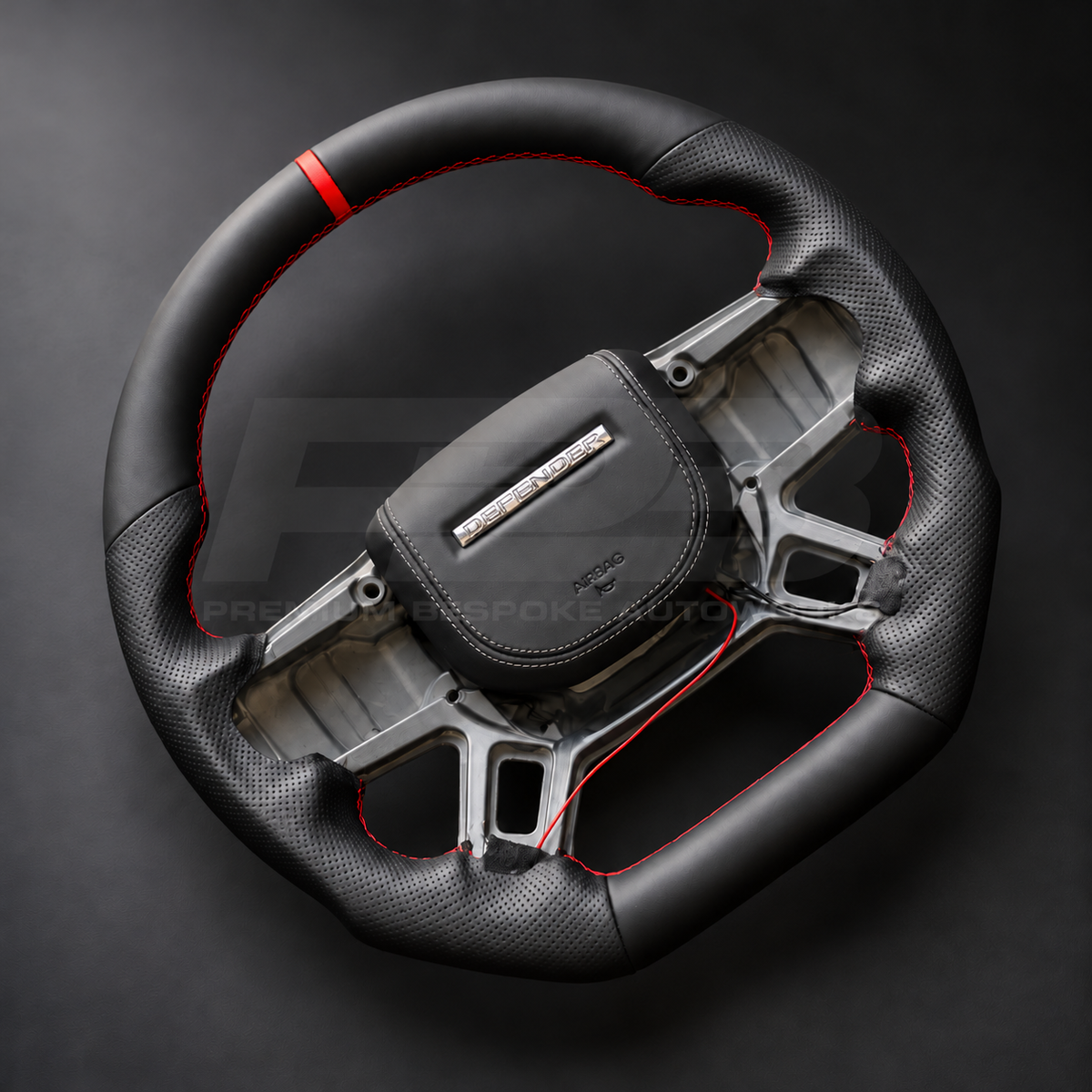 Land Rover Defender L663 custom steering wheel left angle showing flat bottom, black nappa leather, perforated grips, red stitching and red marker, black leather airbag cover