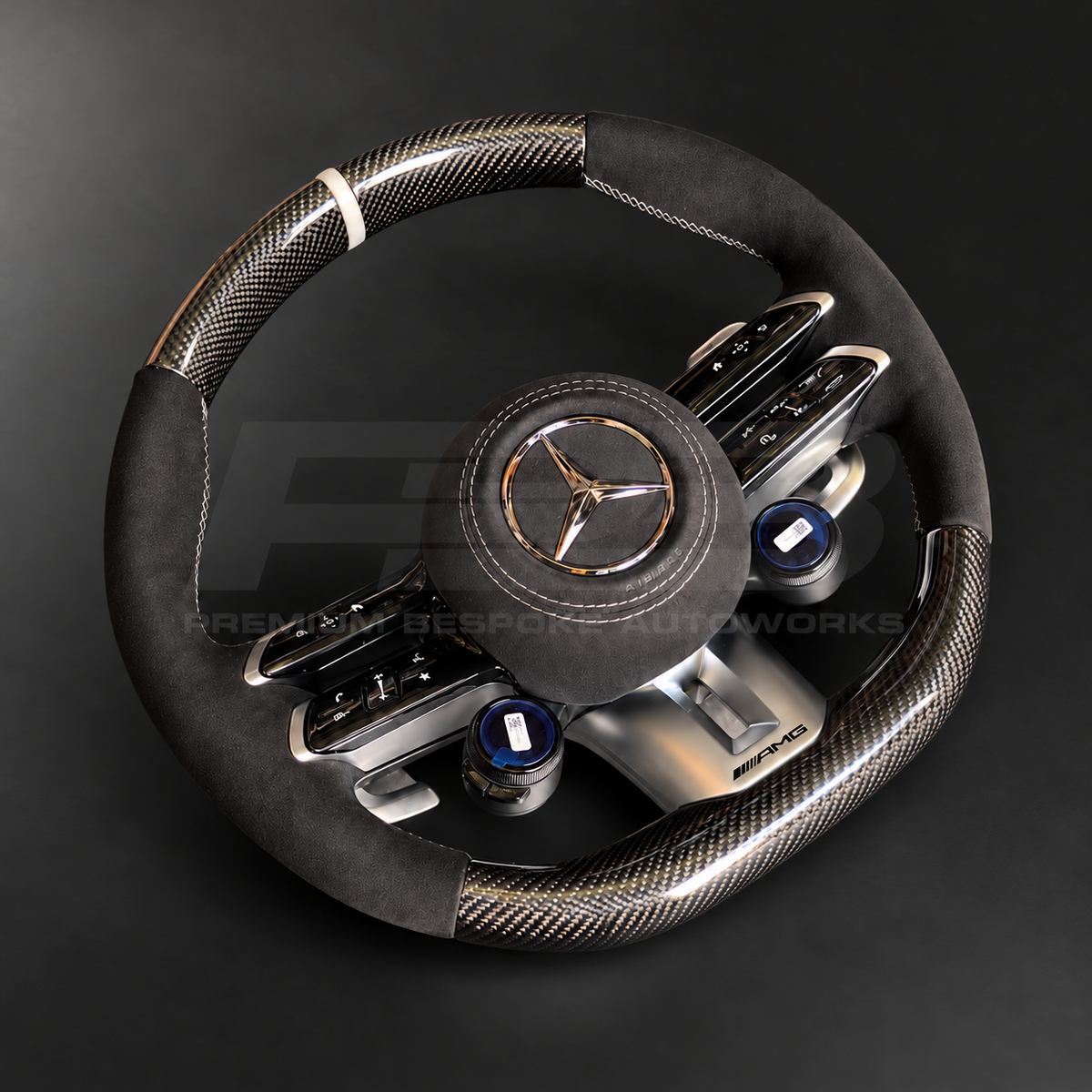 Mercedes-AMG G63 custom steering wheel right angle showing gloss carbon fibre top and bottom, black Alcantara grips and airbag cover, classic grey stitching and marker, AMG drive unit dials