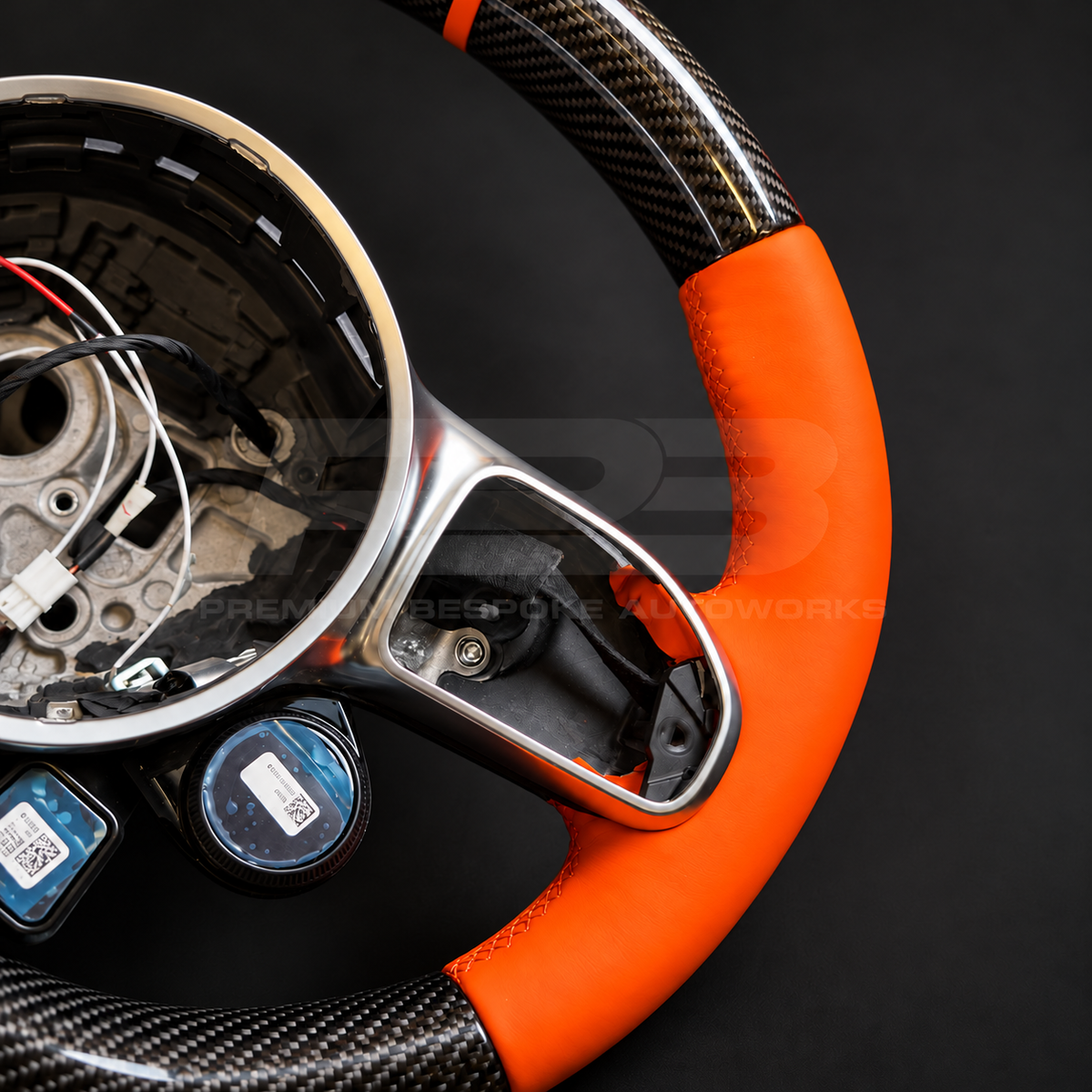 Mercedes-AMG G63 W463 Facelift custom steering wheel close up detail showing gloss carbon fibre top and bottom, orange leather grips and orange 12 o'clock marker