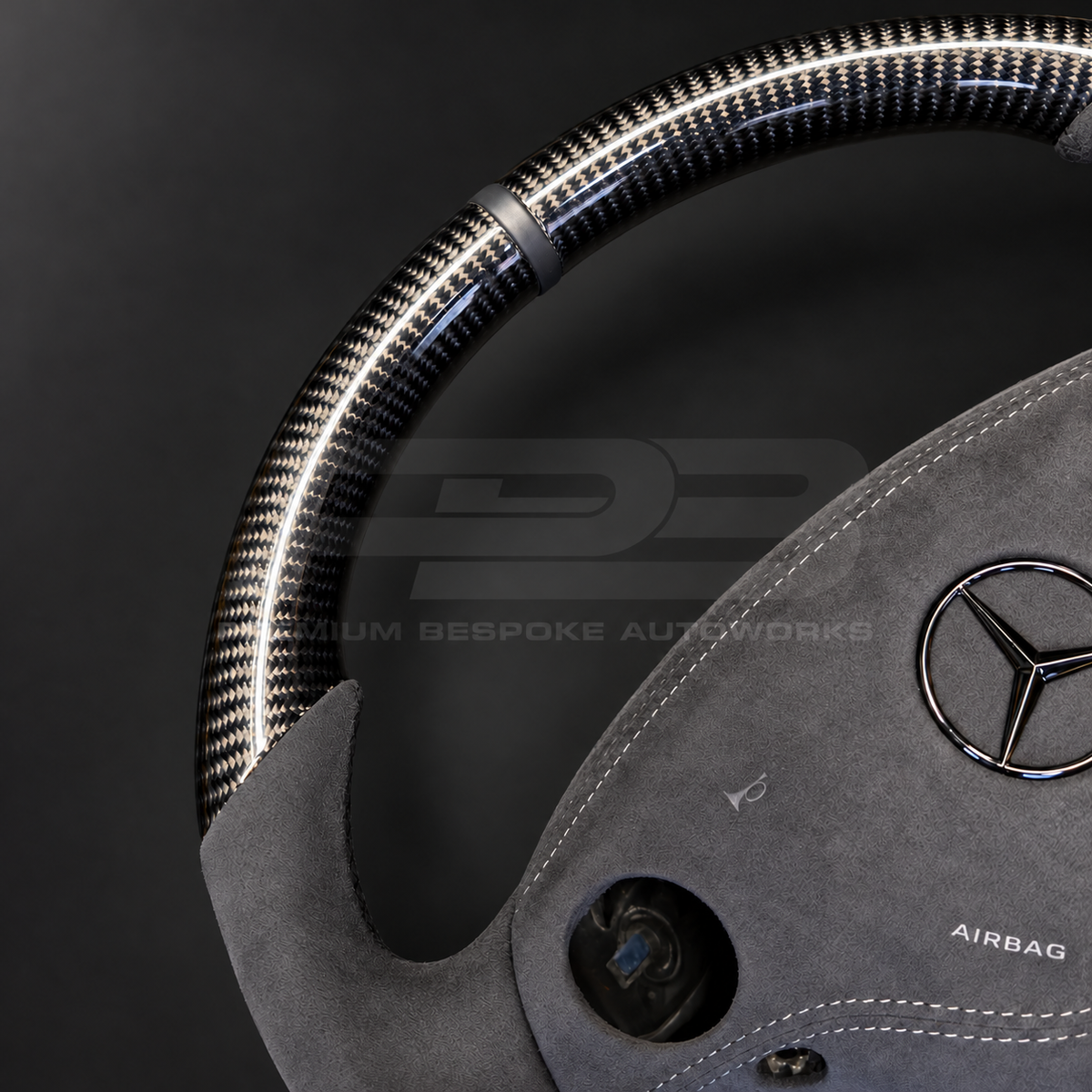Mercedes CL63 AMG C216 custom steering wheel close up detail showing round shape, gloss carbon fibre top, bottom and spokes, dark grey Alcantara grips and airbag cover