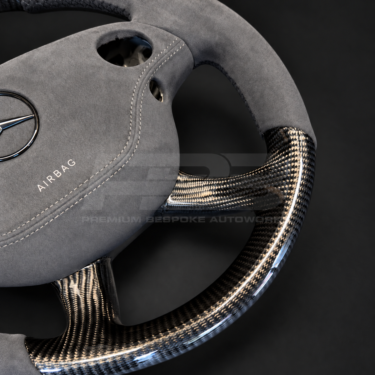 Mercedes CL63 AMG C216 custom steering wheel close up detail showing round shape, gloss carbon fibre top, bottom and spokes, dark grey Alcantara grips and airbag cover