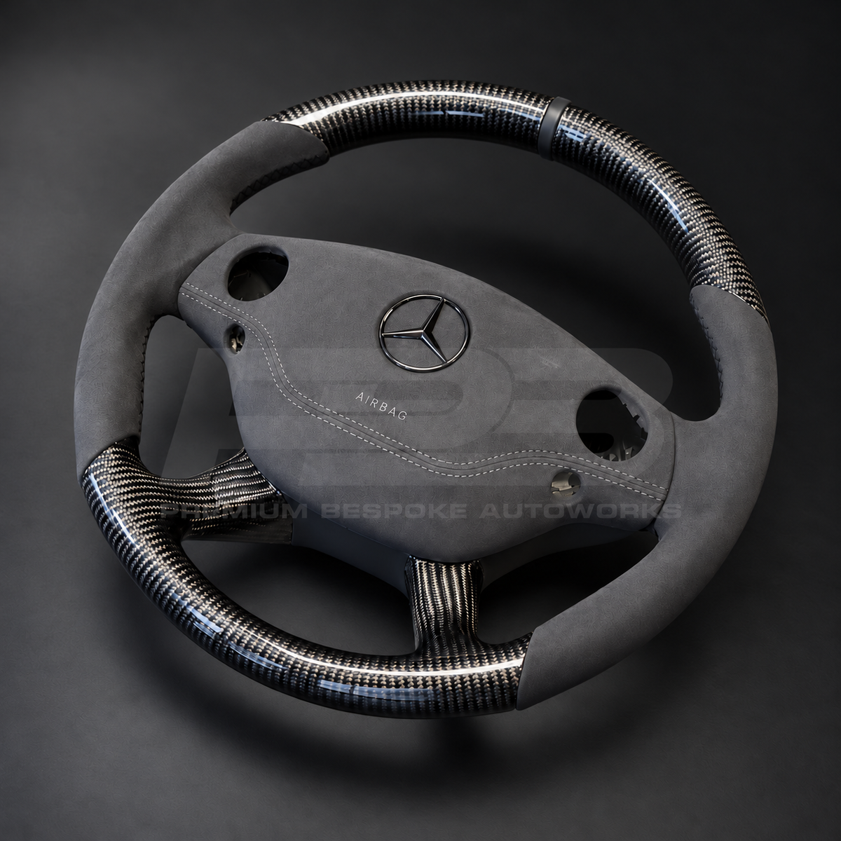 Mercedes CL63 AMG C216 custom steering wheel left angle showing round shape, gloss carbon fibre top, bottom and spokes, dark grey Alcantara grips and airbag cover