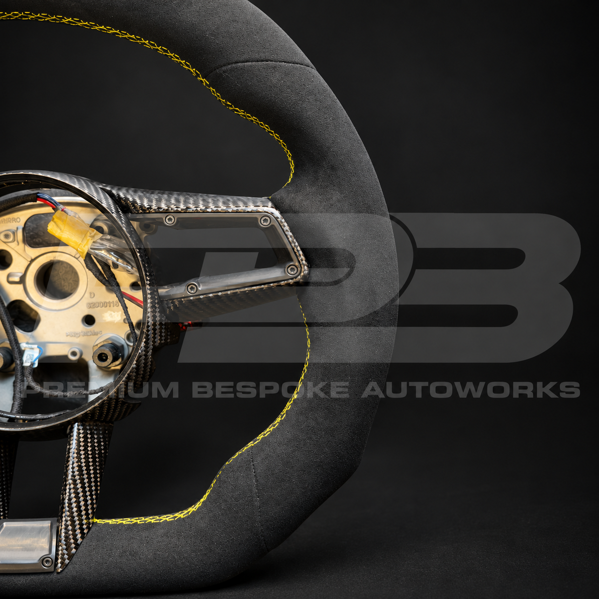 Close up of the yellow stitching and gloss carbon fibre trim on the flat bottom section of a Porsche 911 992 Alcantara custom steering wheel