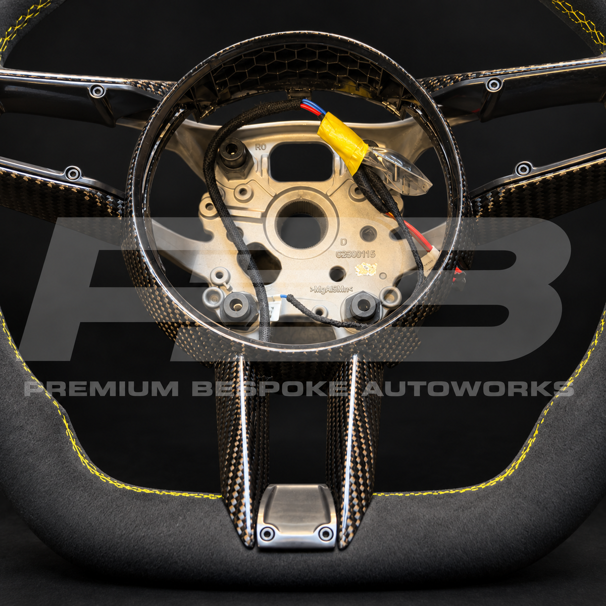 Close up of the gloss carbon fibre spokes and centre trim on a Porsche 911 992 custom steering wheel in black Alcantara with yellow stitching