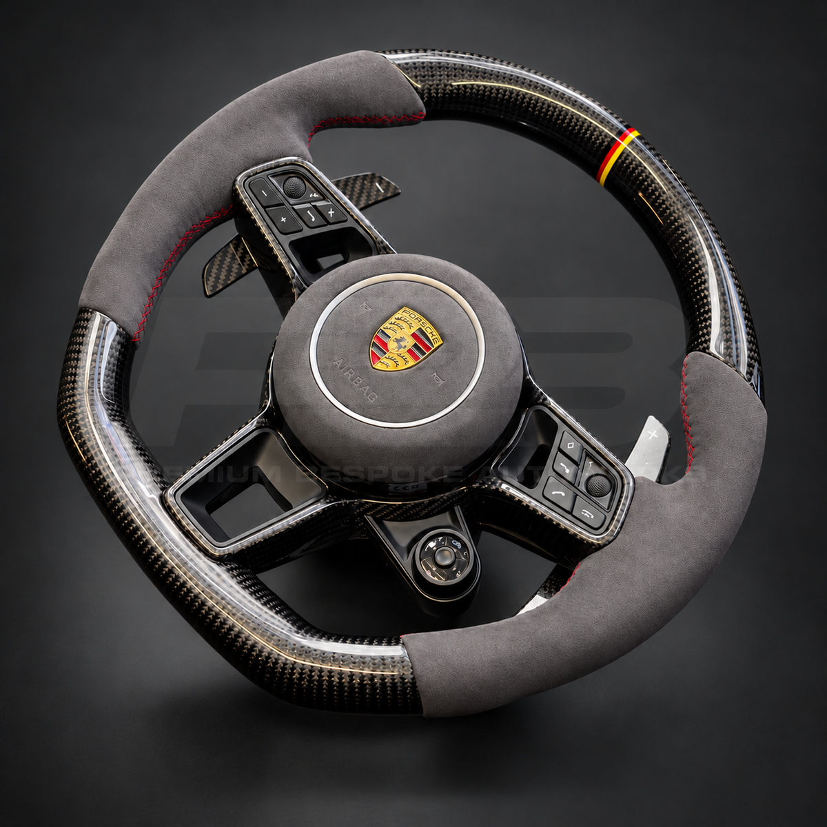 Porsche Cayenne 9Y0 custom steering wheel left angle showing gloss carbon fibre, grey Alcantara grips and airbag cover, red stitching and German flag marker
